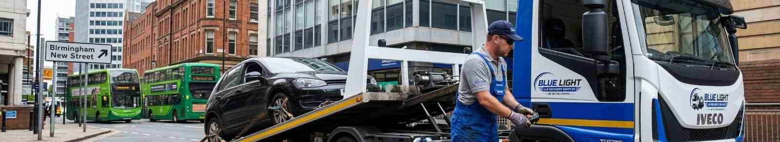 Recovery driver using a remote control to winch a black car onto a Blue Light Car Recovery truck in Birmingham.