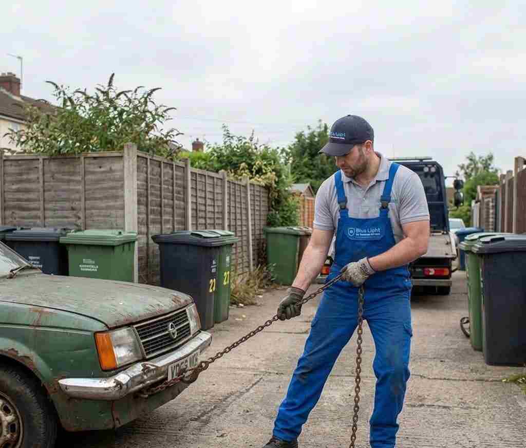 Recovery worker pulling a heavy iron tow chain to hook up an old green Vauxhall Astra in a Northfield back alley.